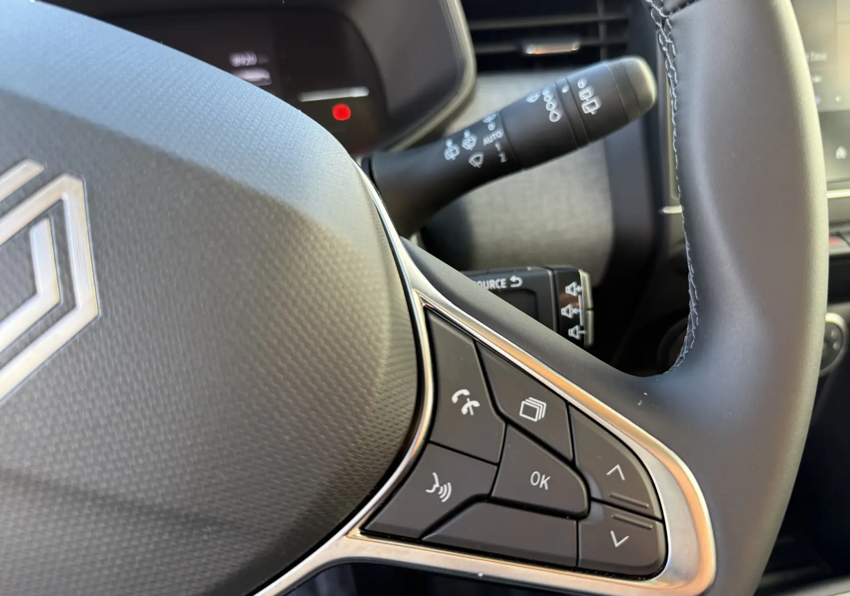 Gros plan sur le volant textile gainé de la Renault Clio V 1.5 dCi 100, avec commandes multifonctions visibles.