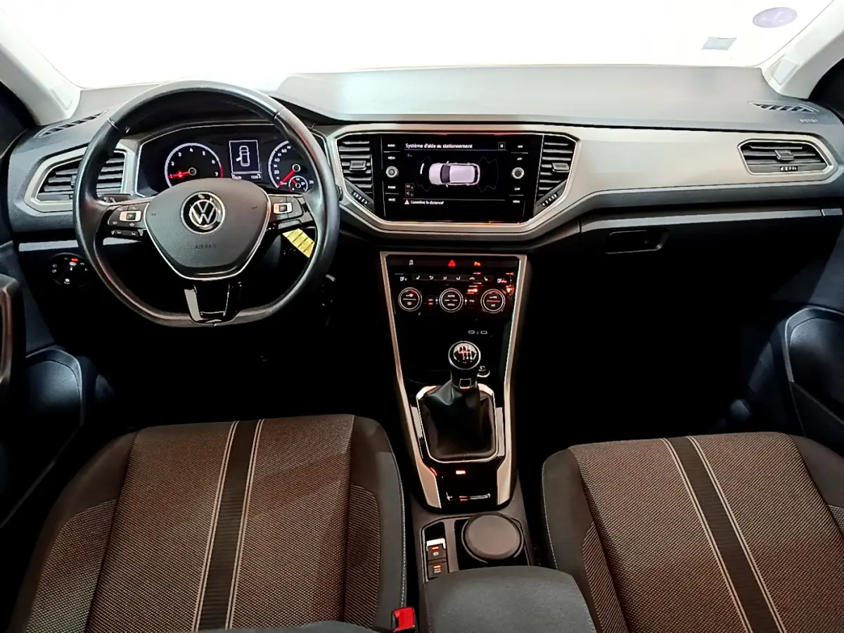 Vue intérieure avant du Volkswagen T-Roc 1.0 TSI 110 Lounge 2021, volant cuir et écran tactile central allumé.