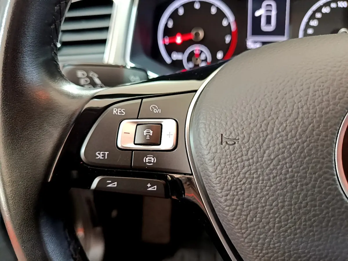 Gros plan sur les commandes du volant cuir du Volkswagen T-Roc 1.0 TSI 110 Lounge, avec tableau de bord en arrière-plan.