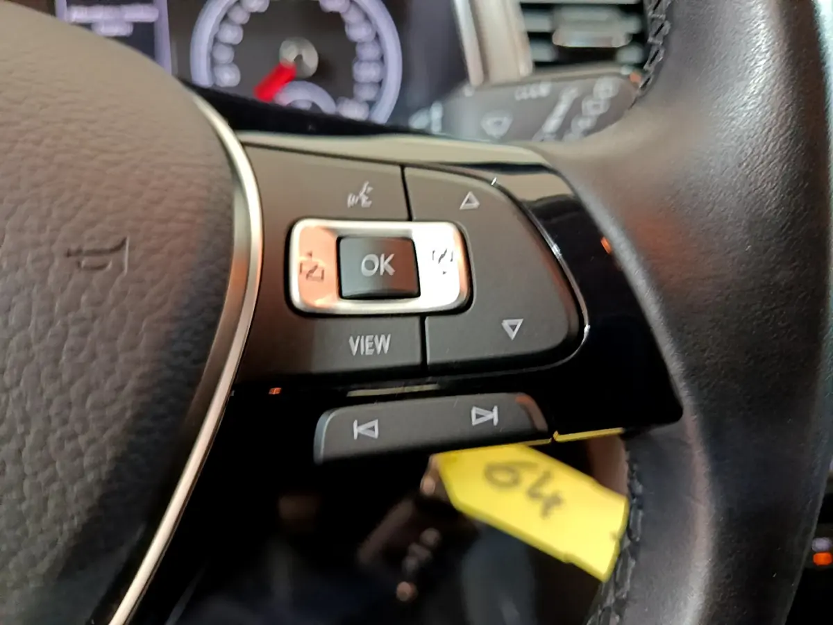 Gros plan sur les commandes gauche du volant cuir noir du Volkswagen T-Roc gris foncé, avec tableau de bord en arrière-plan flou.