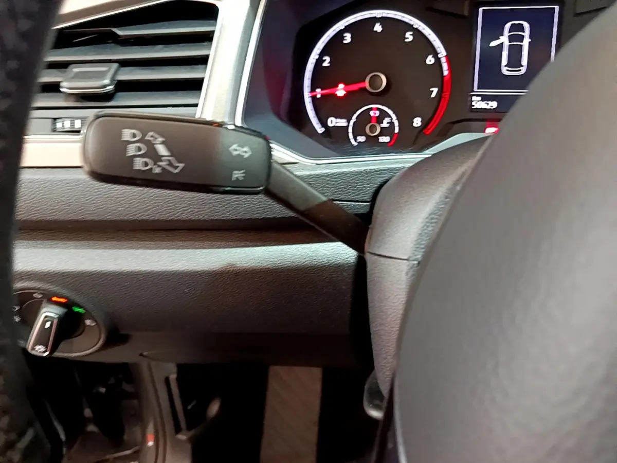 Gros plan sur le tableau de bord et le commodo gauche du Volkswagen T-Roc gris foncé, affichage digital et volant cuir visibles.