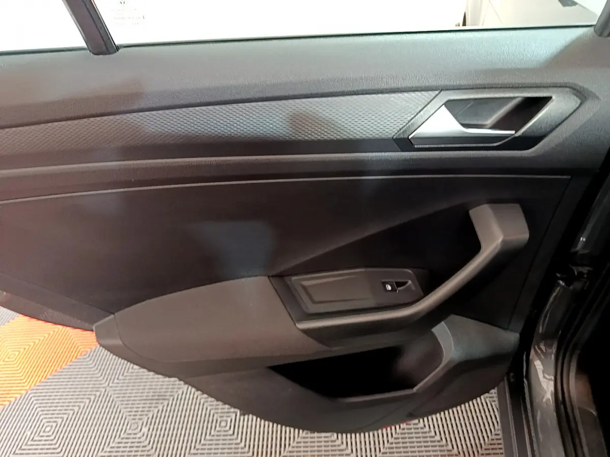 Vue intérieure du panneau de porte côté conducteur du Volkswagen T-Roc gris foncé, avec poignée et commande de vitre électrique.
