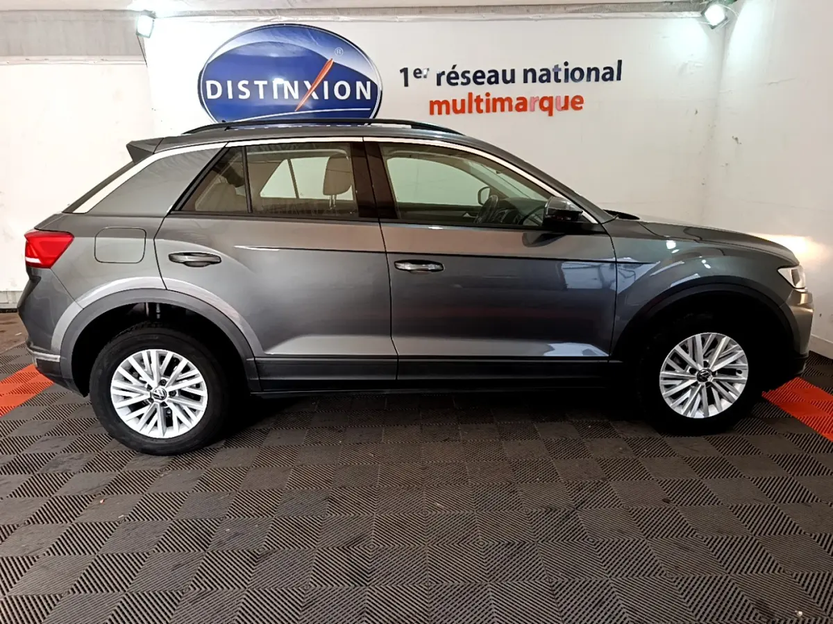 Profil droit d'un Volkswagen T-Roc gris foncé 2021 garé en intérieur avec jantes alliage et barres de toit noires.