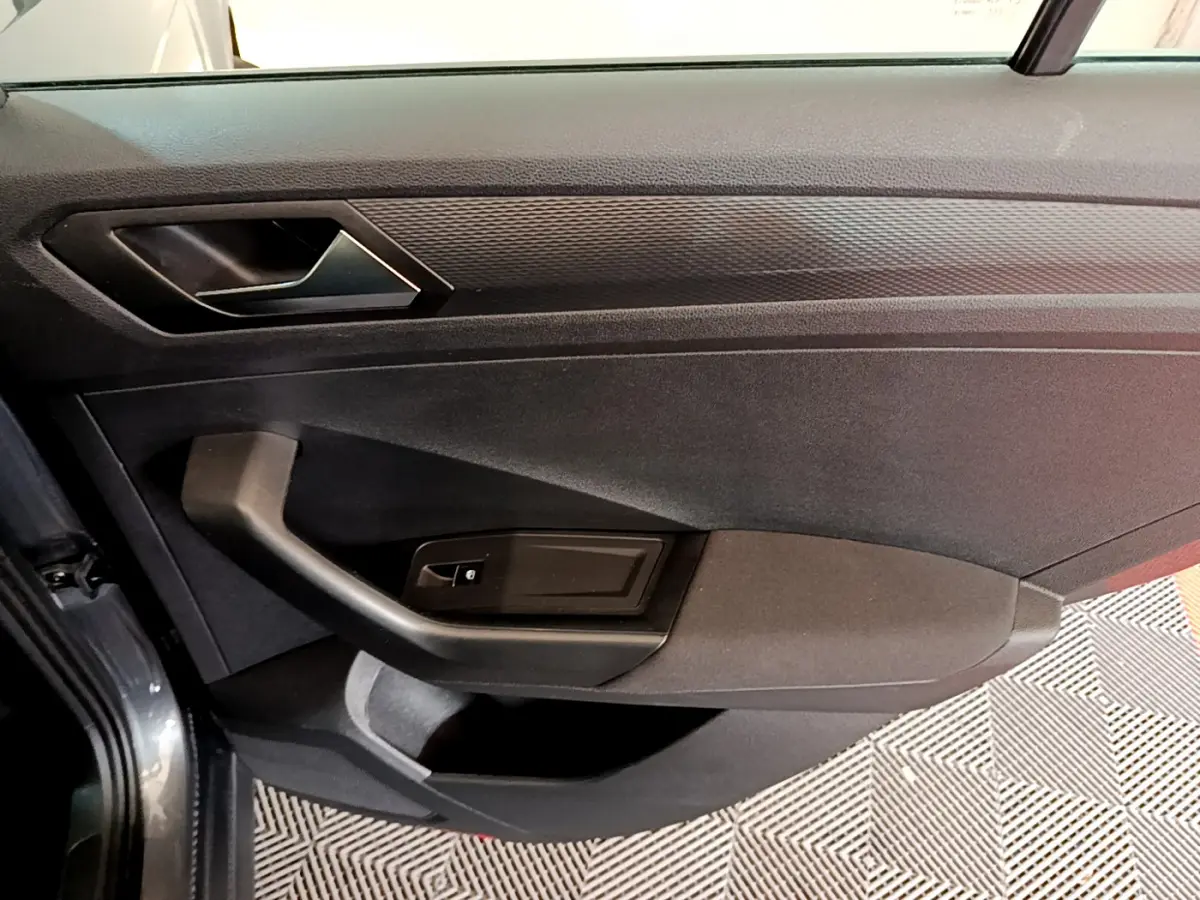 Vue rapprochée de la porte côté gauche du Volkswagen T-Roc gris foncé, mettant en valeur la poignée et les commandes de vitre.