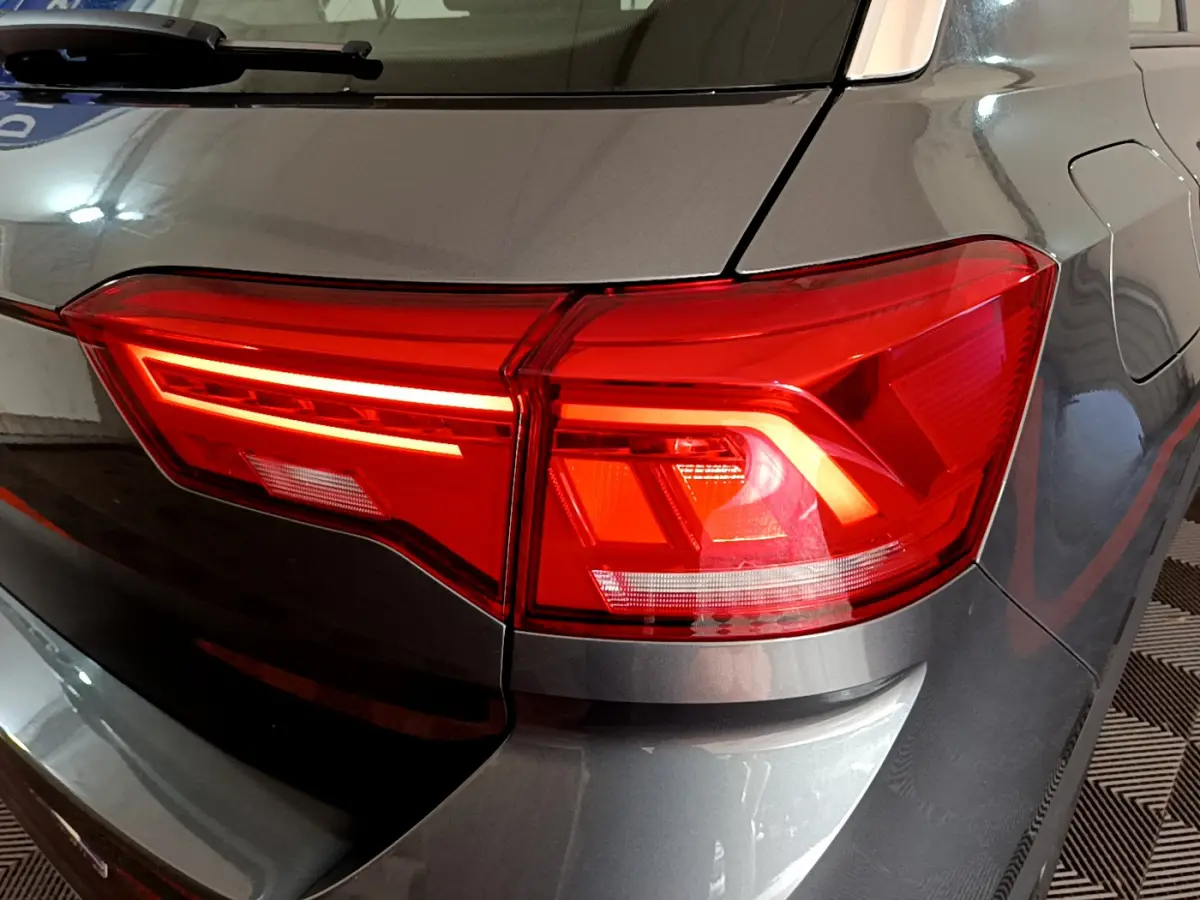 Gros plan sur le feu arrière droit rouge du Volkswagen T-Roc gris foncé, avec reflet sur la carrosserie lisse.