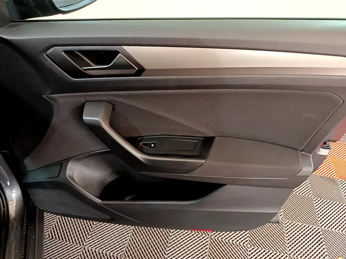Vue rapprochée de la porte intérieure côté conducteur du Volkswagen T-Roc gris foncé avec poignée noire et garniture tissu.