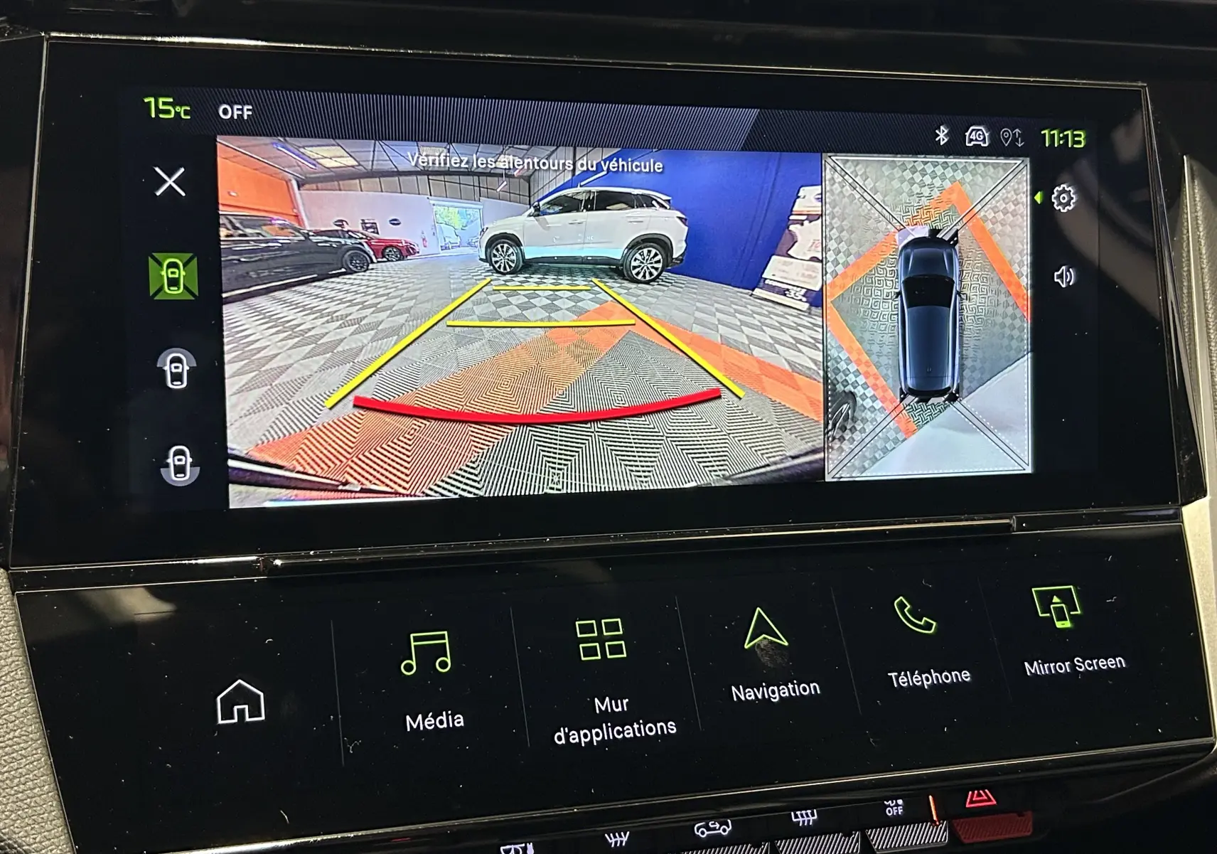 Vue écran intérieur du système Vision 360° montrant une voiture blanche en vue arrière avec lignes de guidage colorées.