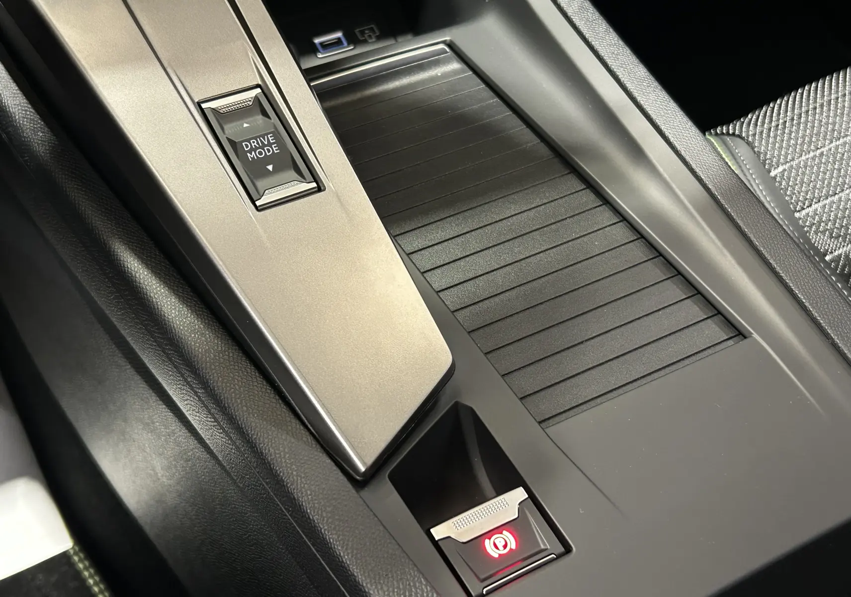 Vue rapprochée de la console centrale noire de la Peugeot 308 III Ph.2 GT avec bouton Drive Mode et frein à main électrique.