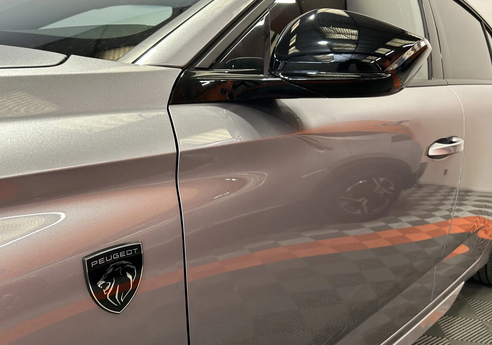 Gros plan sur le côté gauche gris Artense d’une Peugeot 308 III Ph.2 GT avec logo lion et rétroviseur noir brillant.