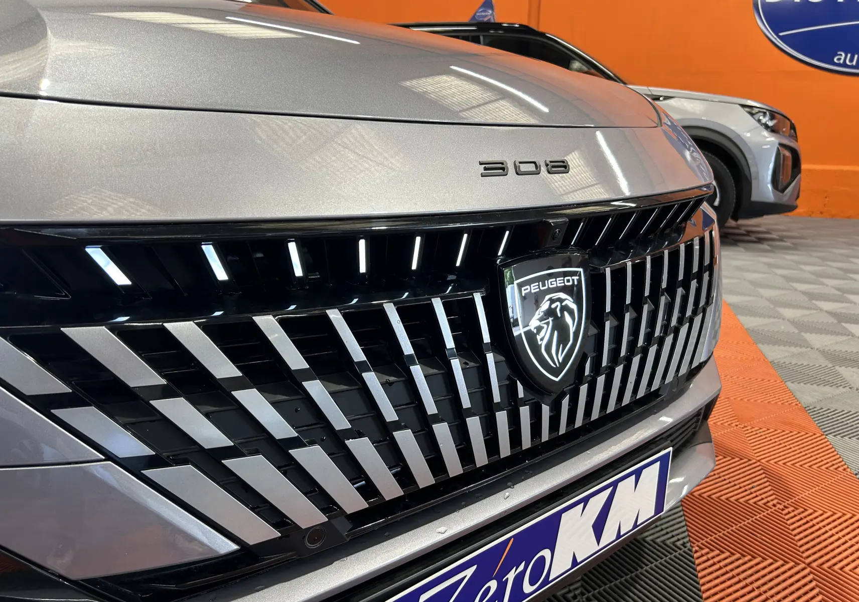 Gros plan sur la calandre avant gris Artense de la Peugeot 308 III Ph.2 GT avec logo lion et inscription 308.