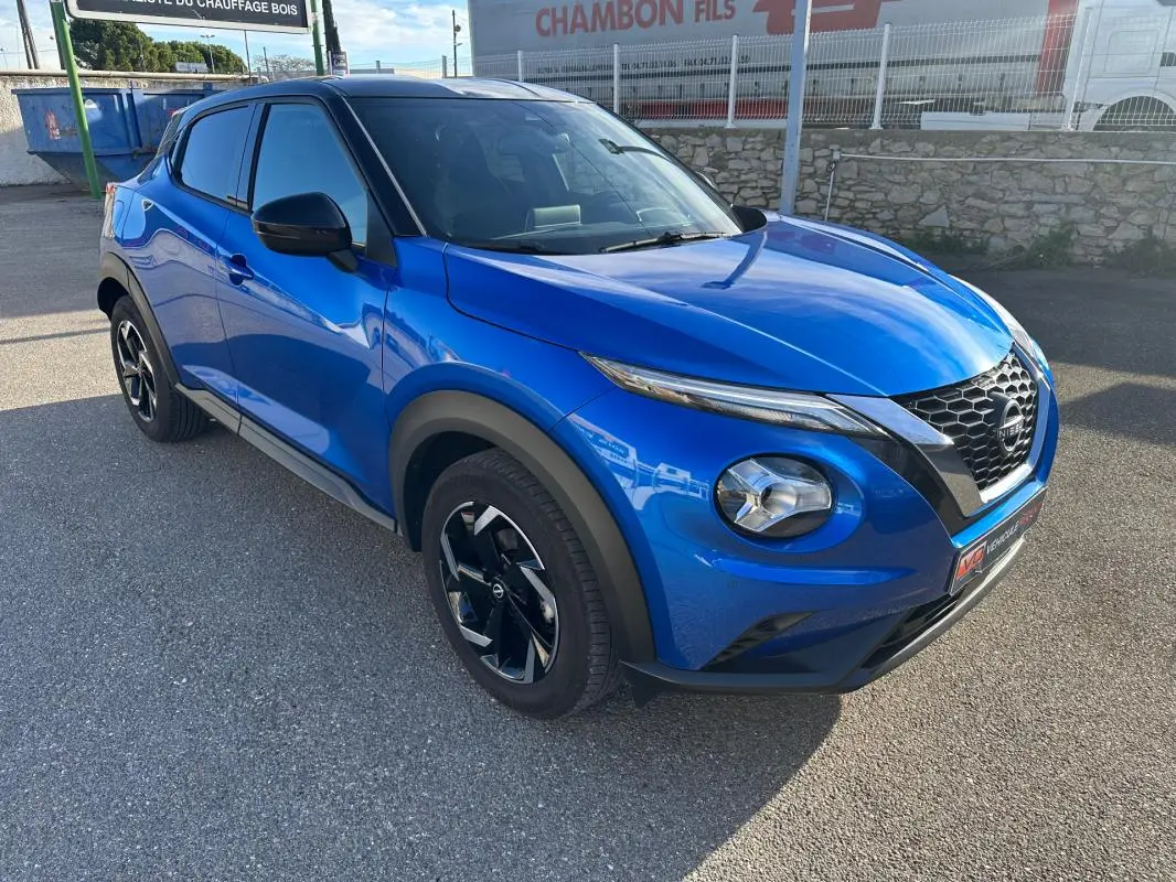 Nissan Juke 2024 bleu clair en 3/4 avant droit, avec jantes alliage noires et calandre en V distinctive.