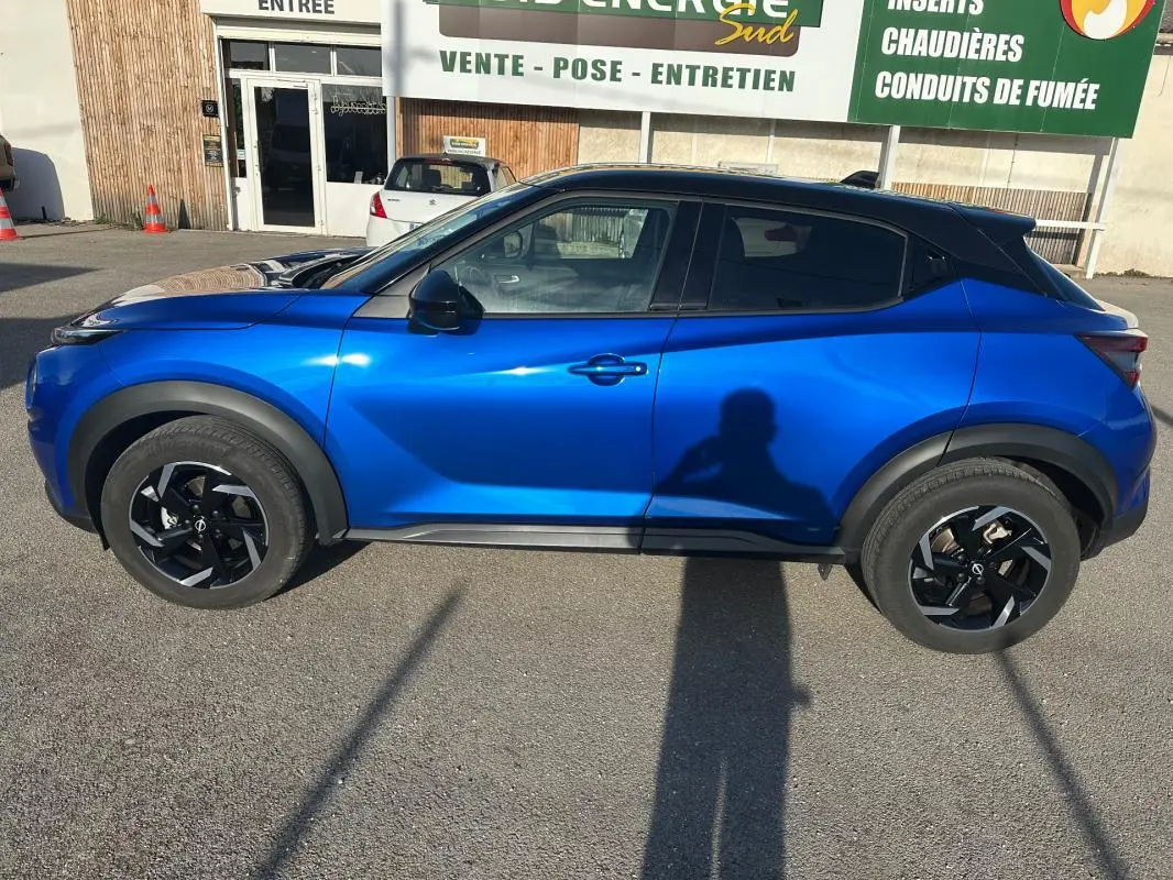 Vue de profil côté gauche d'un Nissan Juke 2024 bleu clair avec jantes alliage noires de 17 pouces sur parking.