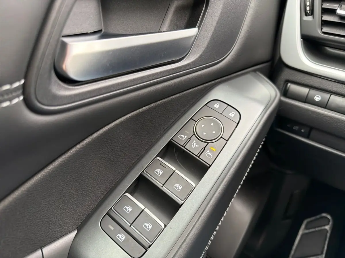 Gros plan sur la commande des vitres et rétroviseurs côté conducteur du Nissan Qashqai noir, intérieur noir avec surpiqûres blanches.