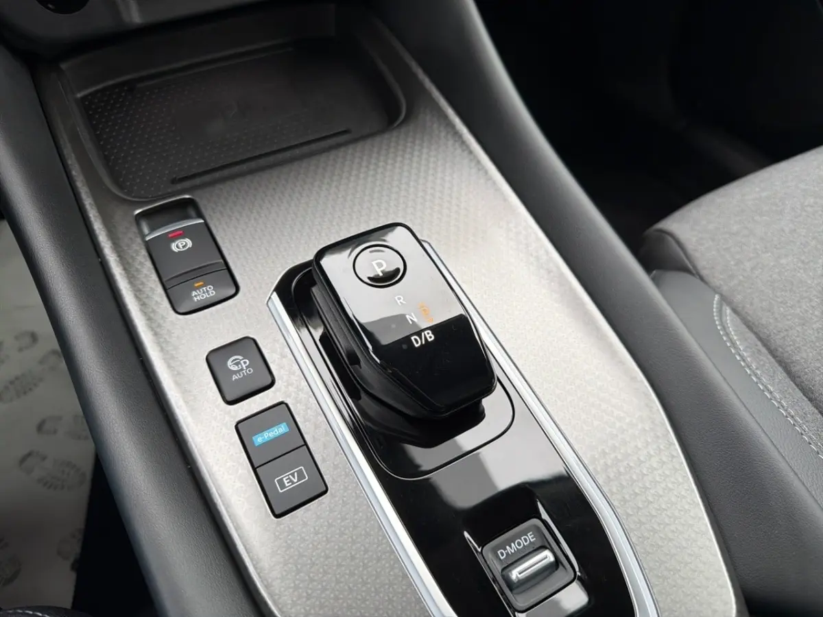 Gros plan sur la console centrale noire et grise du Nissan Qashqai 1.5 e-Power avec levier de vitesses automatique et boutons fonctionnels.