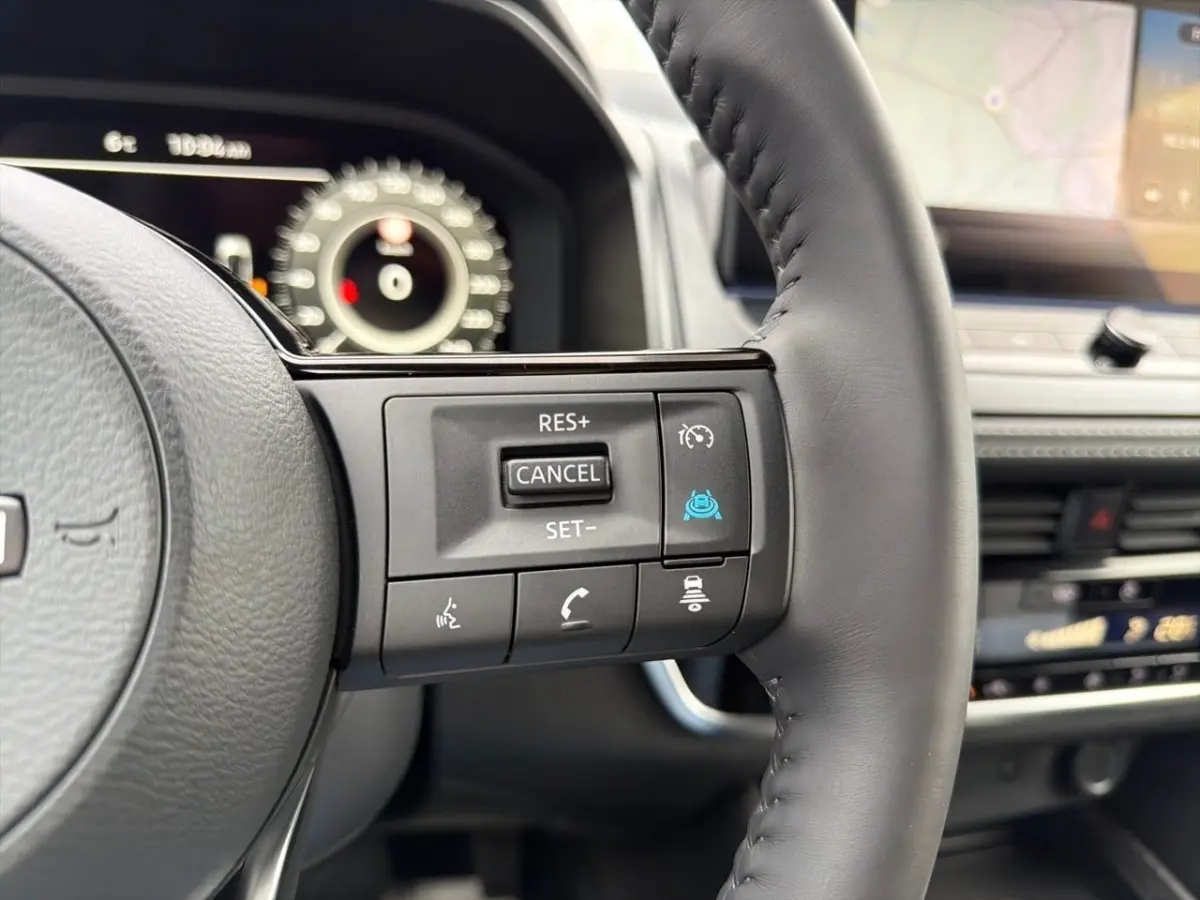 Gros plan sur les commandes au volant cuir noir du Nissan Qashqai 1.5 e-Power 2025, avec tableau de bord numérique en arrière-plan.
