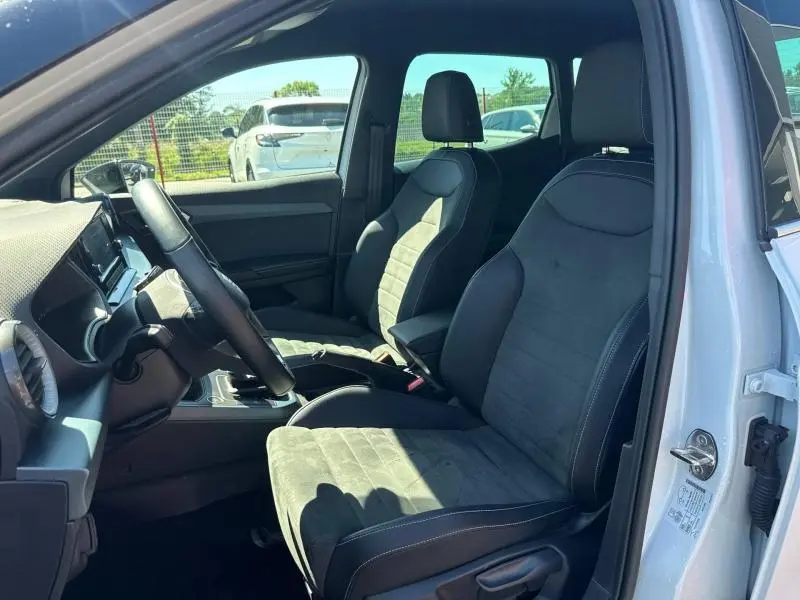 Vue intérieure côté conducteur du SEAT Arona blanc Nevada, sièges tissu gris Sano avec volant cuir multifonction.