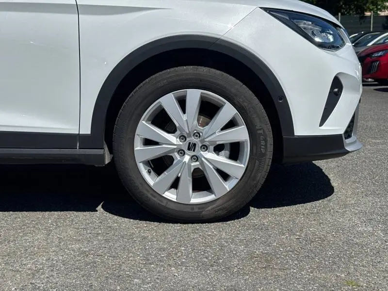 Gros plan sur la roue avant gauche d'une SEAT Arona blanche Nevada Métal avec jante alu et partie avant visible.