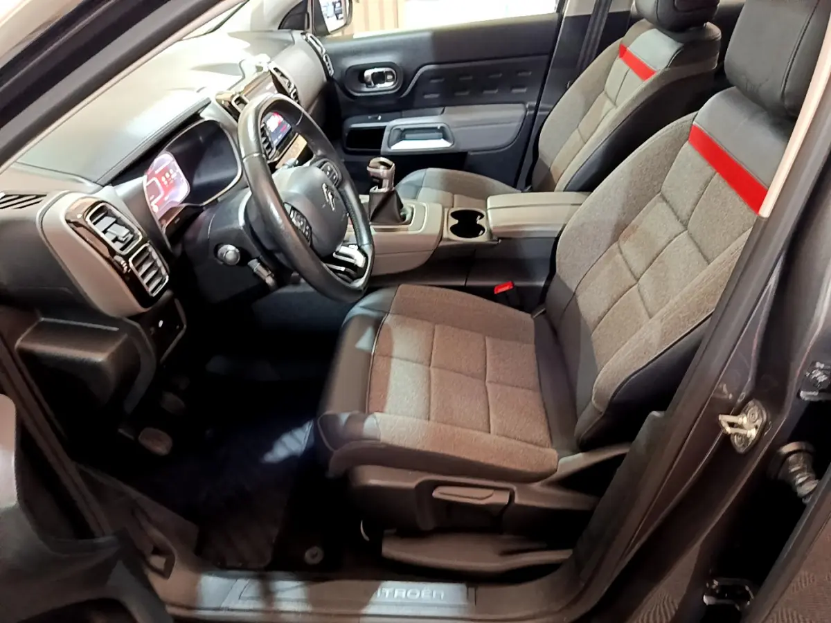Intérieur avant droit du Citroën C5 Aircross gris foncé, sièges tissu gris avec bande rouge et volant cuir noir.