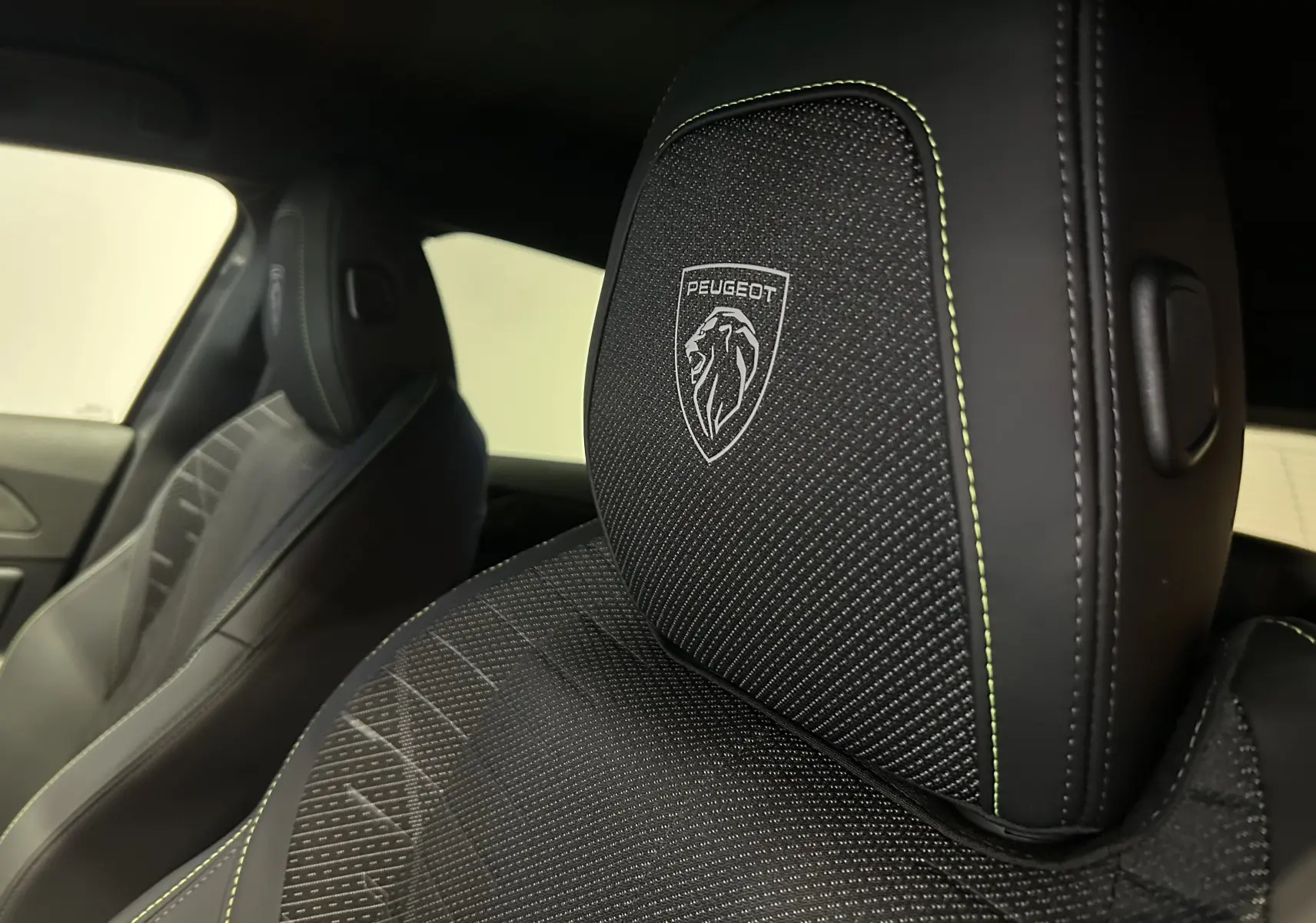 Gros plan sur l’appui-tête avant droit noir avec logo Peugeot et surpiqûres vertes dans l’habitacle.