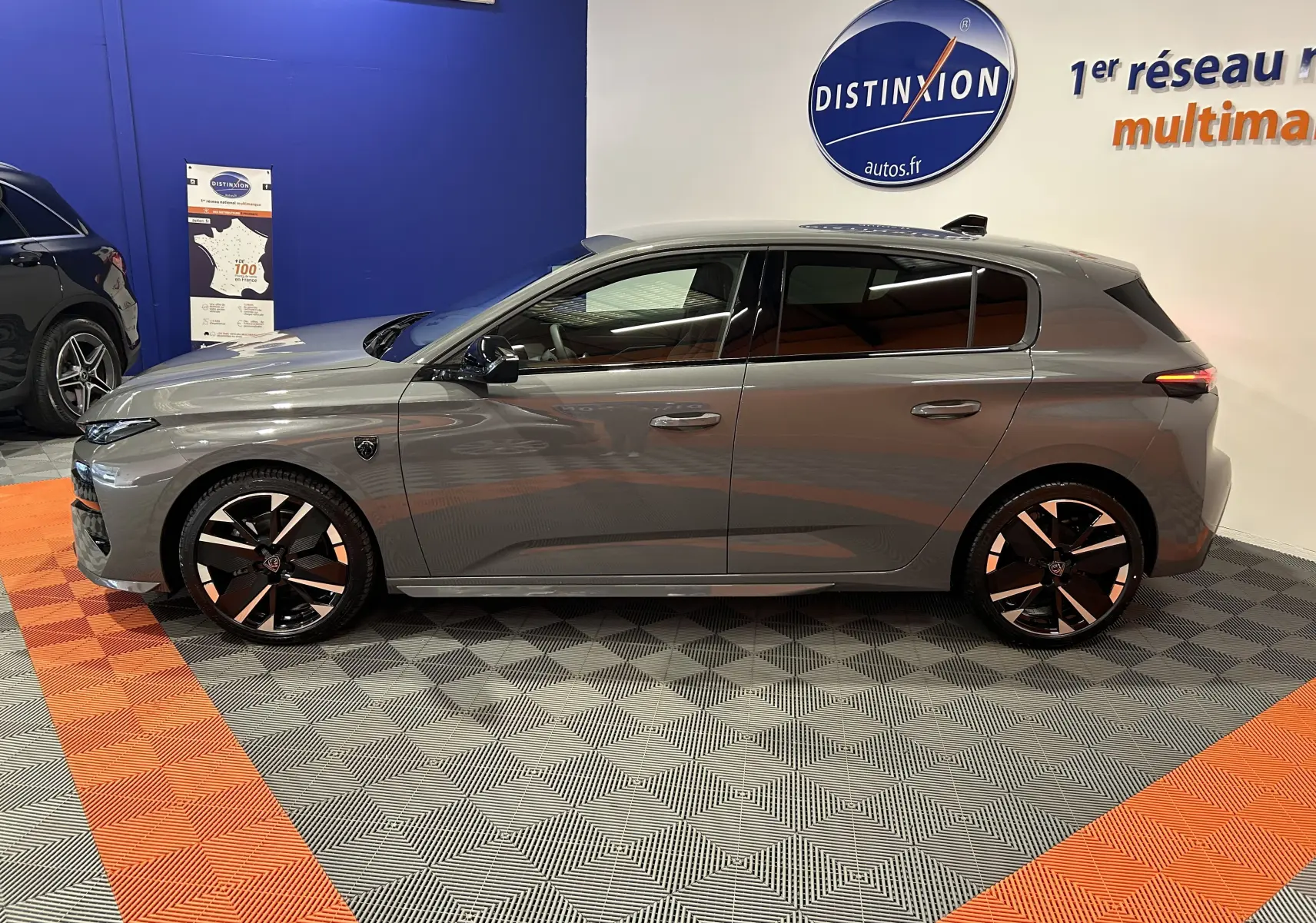 Profil droit de la Peugeot 308 III Ph.2 HYBRID 145 GT gris Selenium, avec jantes noires et détails modernes en showroom.