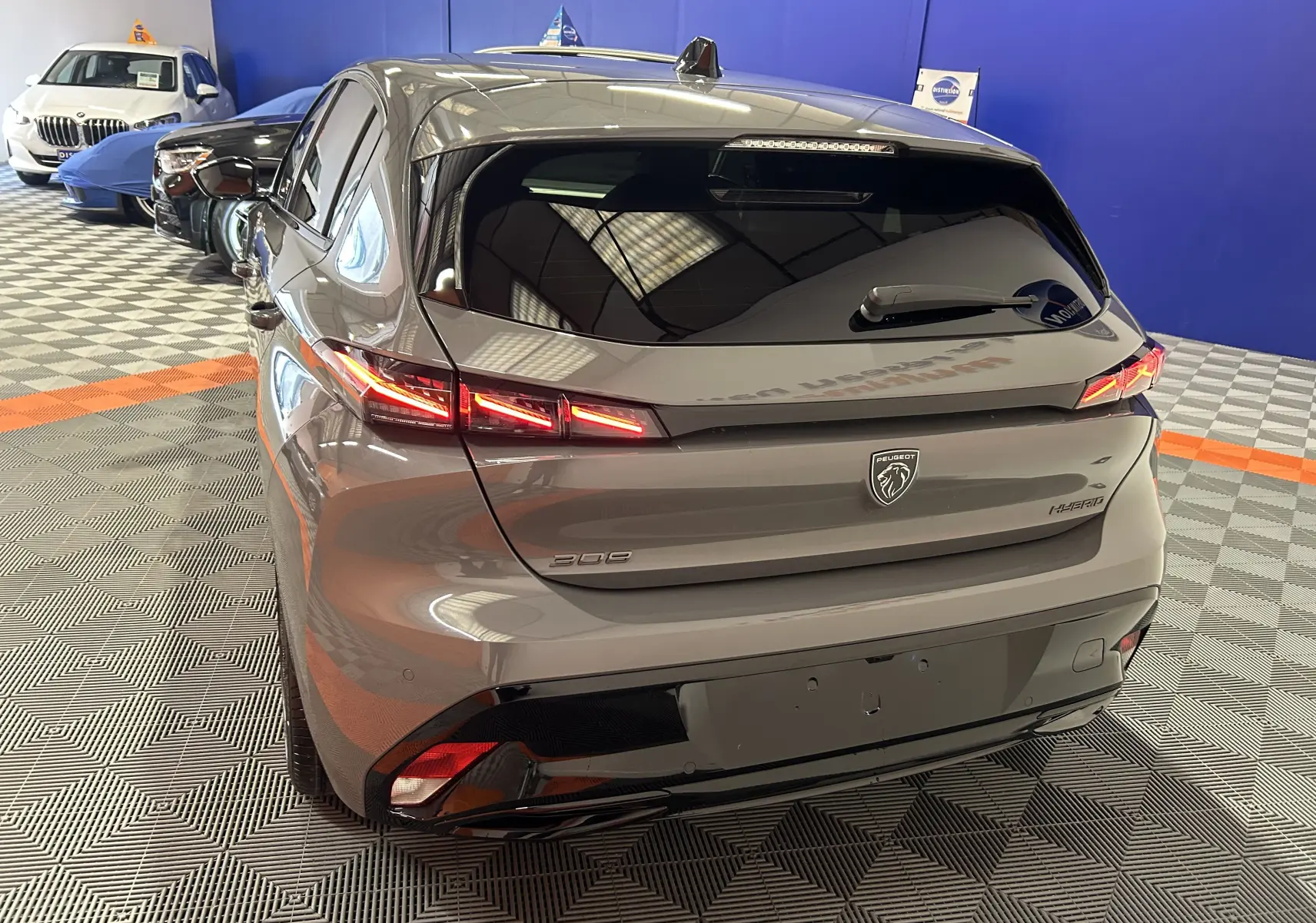 Vue 3/4 arrière droite d'une Peugeot 308 III Ph.2 Hybrid 145 GT gris Selenium avec feux arrière LED allumés.