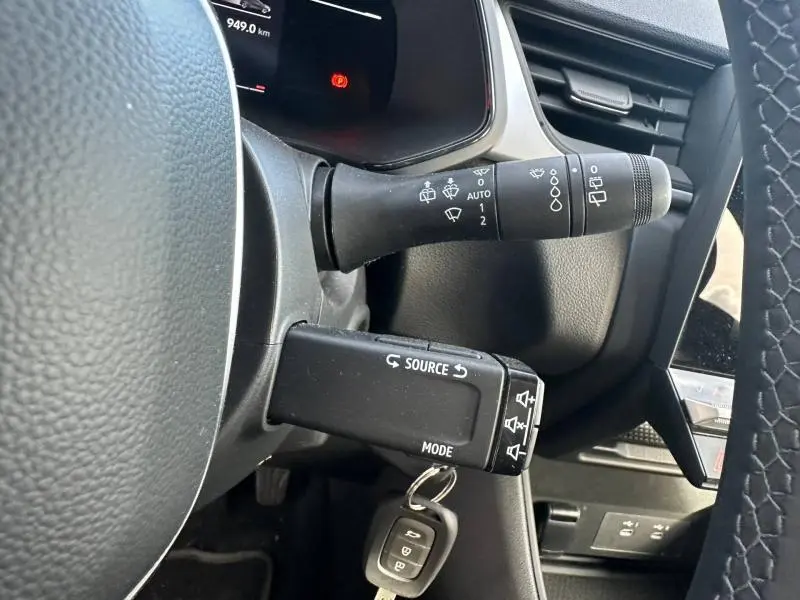 Gros plan sur les commandes au volant noir du Renault Captur blanc nacré 2025, avec clé insérée et tableau de bord partiel.