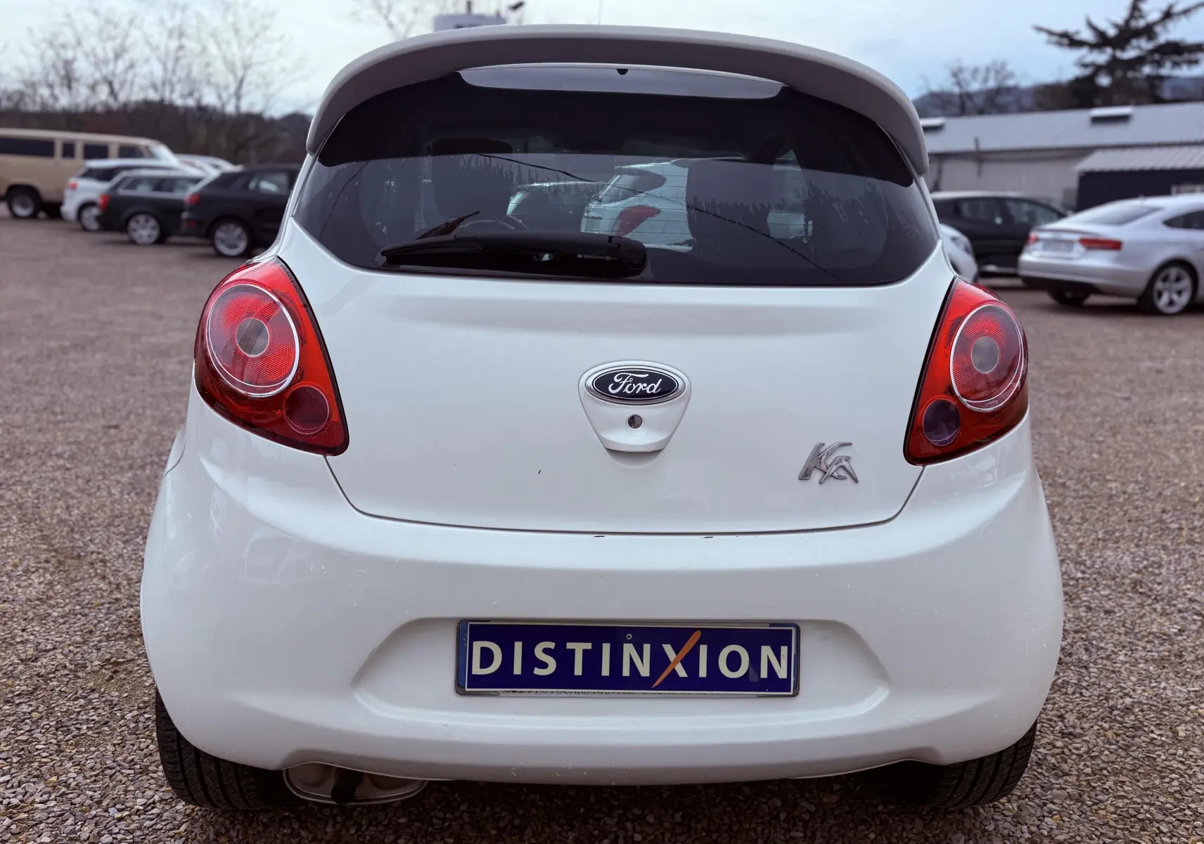 Vue arrière d'une Ford Ka blanche de 2015 avec feux rouges et plaque d'immatriculation Distinxion visible.