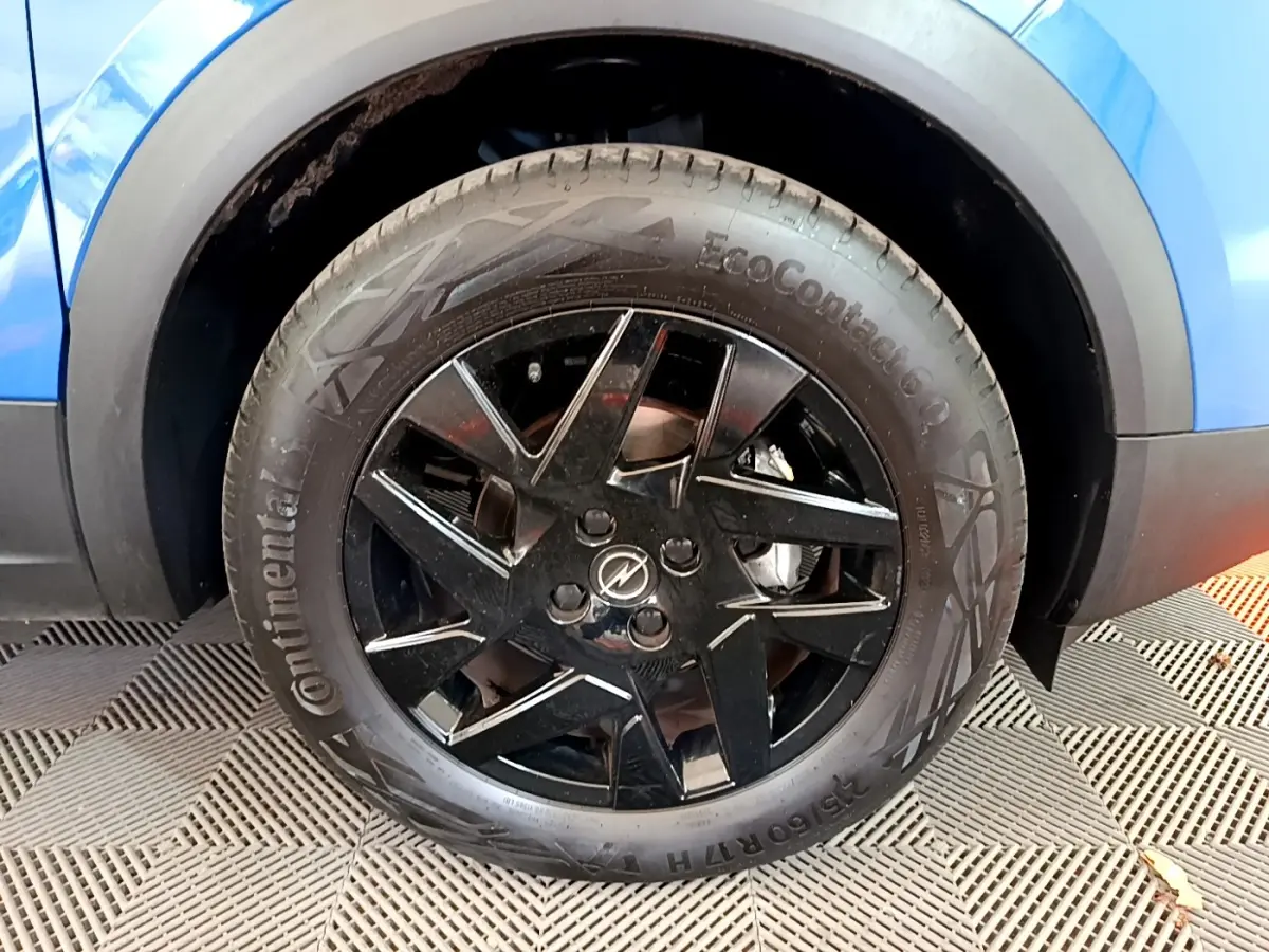 Gros plan sur la roue avant droite noire brillante d’un Opel Mokka bleu 2024 avec jante en alliage.