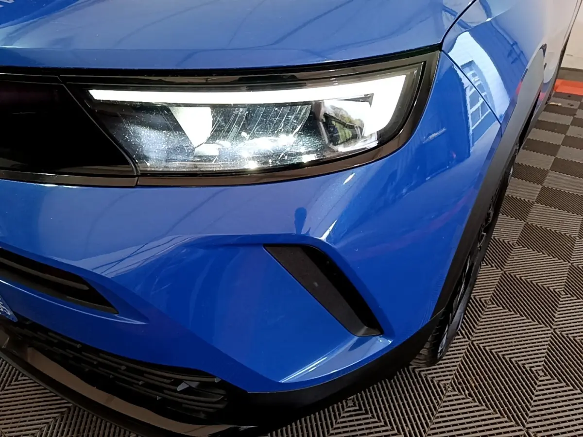 Gros plan sur l'avant droit bleu de l'Opel Mokka 2024, mettant en valeur le phare LED et la calandre noire.