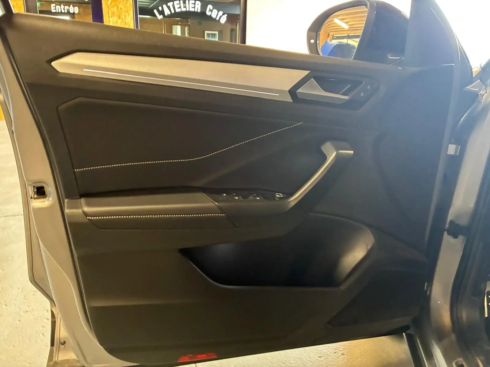 Vue intérieure de la porte avant gauche du Volkswagen T-Roc gris clair, avec garniture noire et surpiqûres claires.
