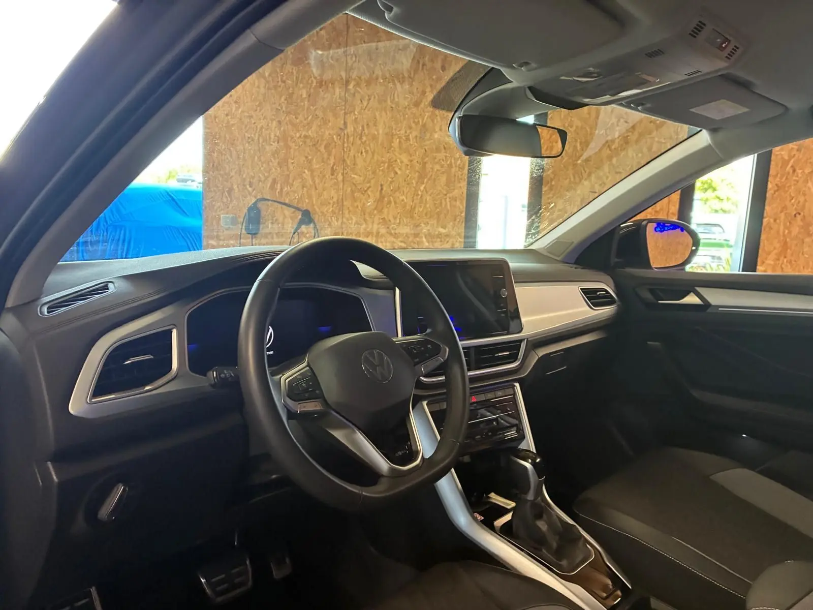 Vue intérieure côté conducteur du Volkswagen T-Roc gris clair 2025, avec volant multifonction et écran tactile central.