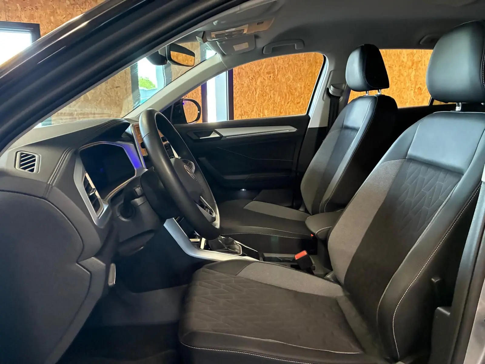 Vue intérieure côté conducteur du Volkswagen T-Roc 2025, montrant les sièges tissu noir et la planche de bord moderne.