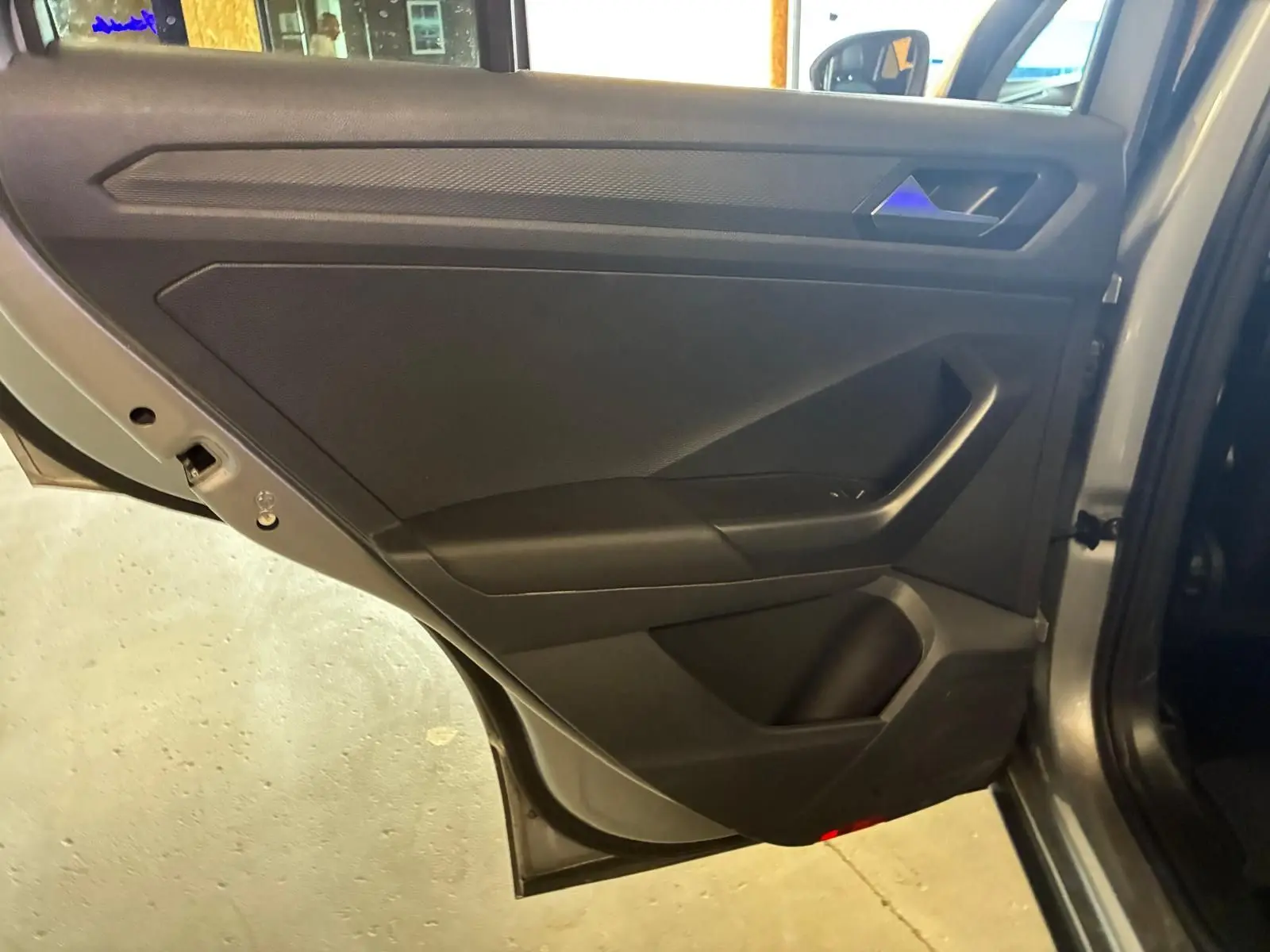 Vue intérieure de la porte arrière droite du Volkswagen T-Roc gris clair, montrant le panneau de porte noir avec poignée intégrée.