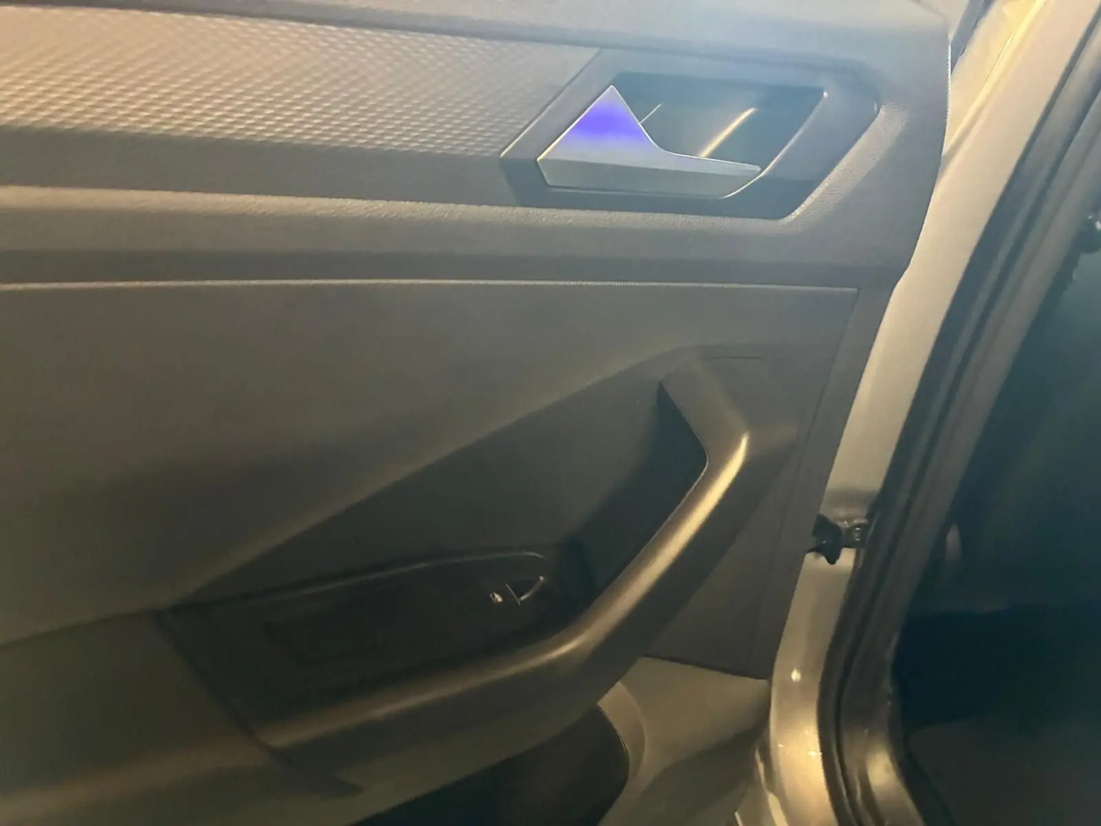 Détail de la porte intérieure côté gauche du Volkswagen T-Roc gris clair, avec poignée et commande de vitre.
