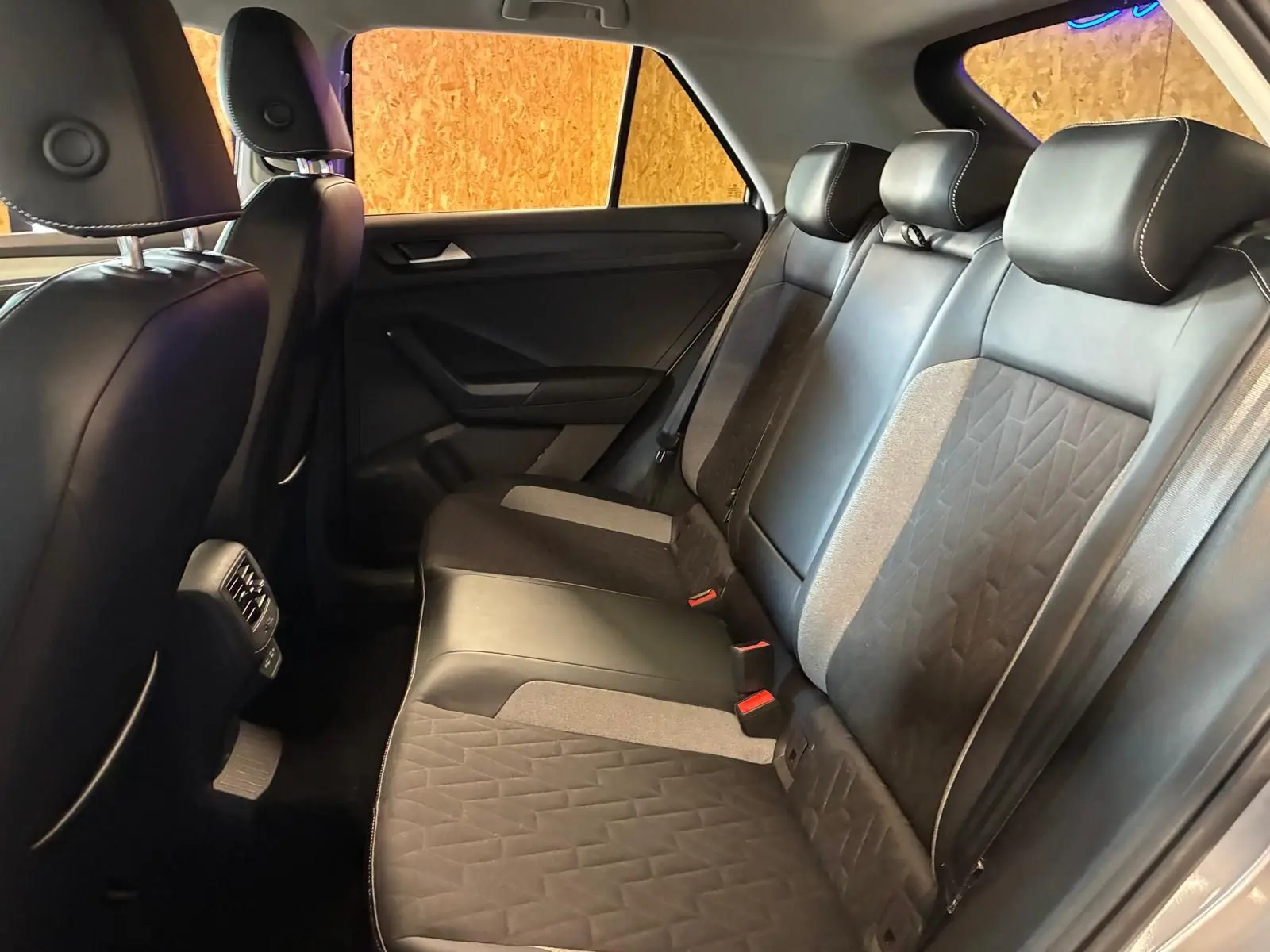 Vue intérieure arrière du Volkswagen T-Roc 2025 montrant les sièges en tissu noir et gris avec appuie-têtes et ceinture de sécurité.