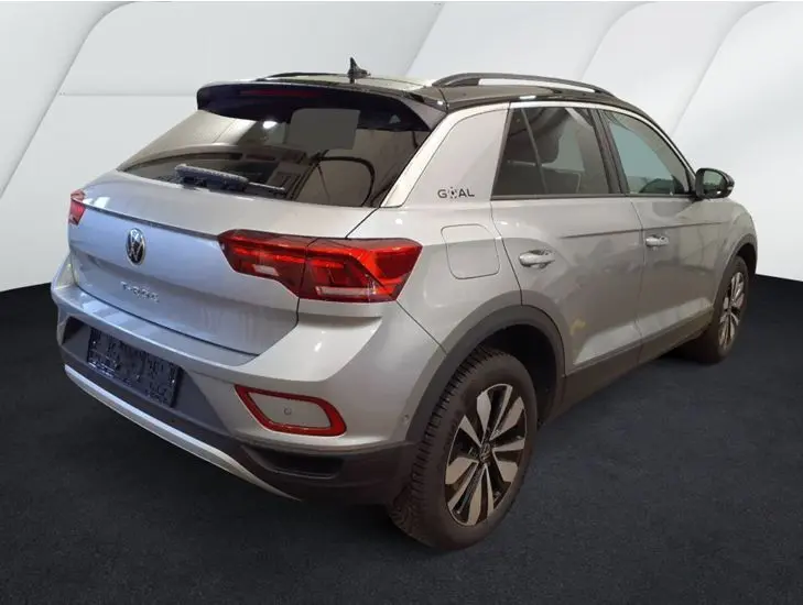 Vue 3/4 arrière droite d’un Volkswagen T-Roc gris clair 2025 avec toit noir et jantes alliage distinctives.