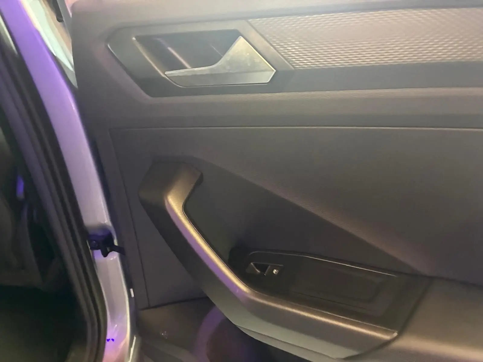 Gros plan sur la porte intérieure côté gauche du Volkswagen T-Roc gris clair, mettant en valeur la poignée et les commandes.