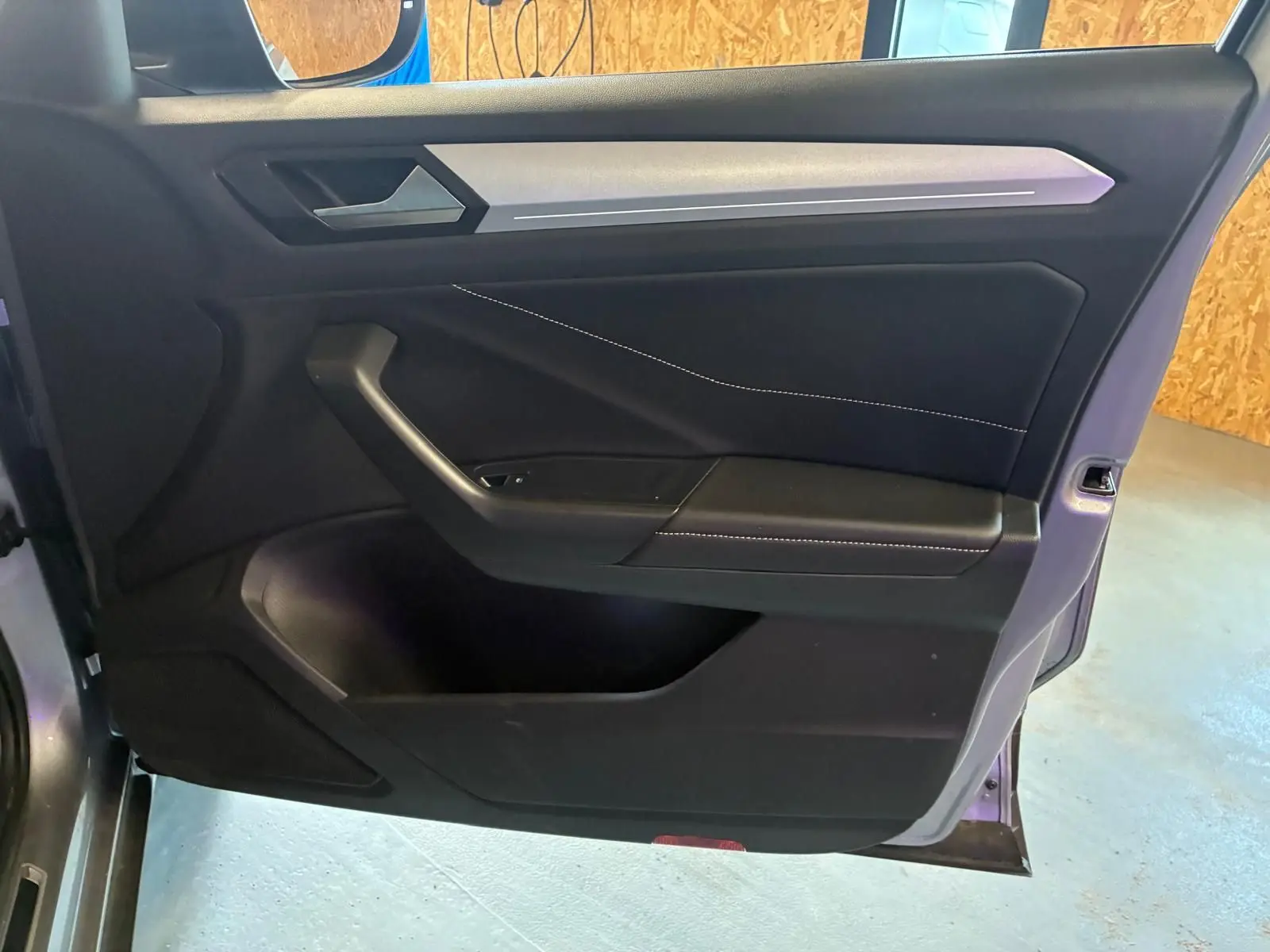 Vue intérieure de la porte avant gauche du Volkswagen T-Roc gris clair, avec garniture noire et surpiqûres blanches.