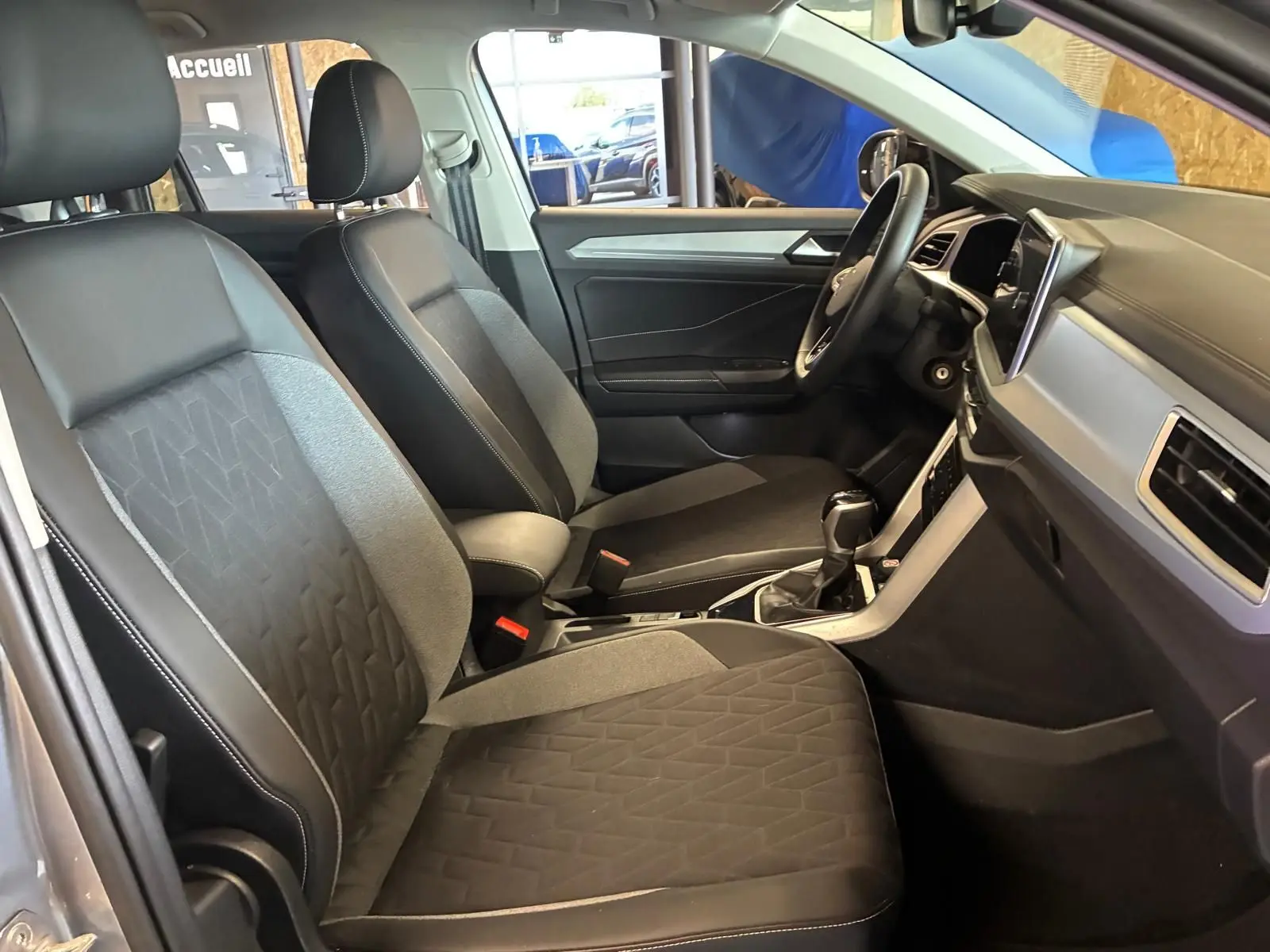 Vue intérieure côté gauche du Volkswagen T-Roc 2025, sièges tissu gris foncé avec motifs géométriques et tableau de bord moderne.