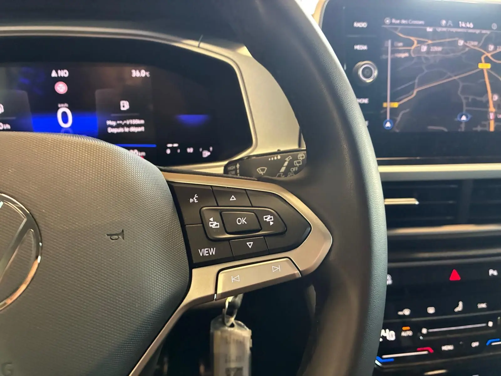 Vue rapprochée du volant noir du Volkswagen T-Roc 2025 avec commandes intégrées et écran numérique en arrière-plan.