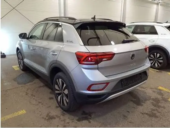 Vue 3/4 arrière droite d’un Volkswagen T-Roc gris clair 2025 avec toit noir et feux arrière LED dans un garage.