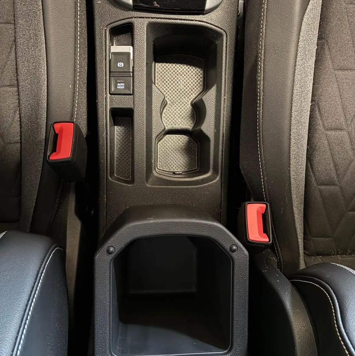 Vue plongeante sur la console centrale noire du Volkswagen T-Roc 2025 avec porte-gobelets et boutons de frein à main électronique.