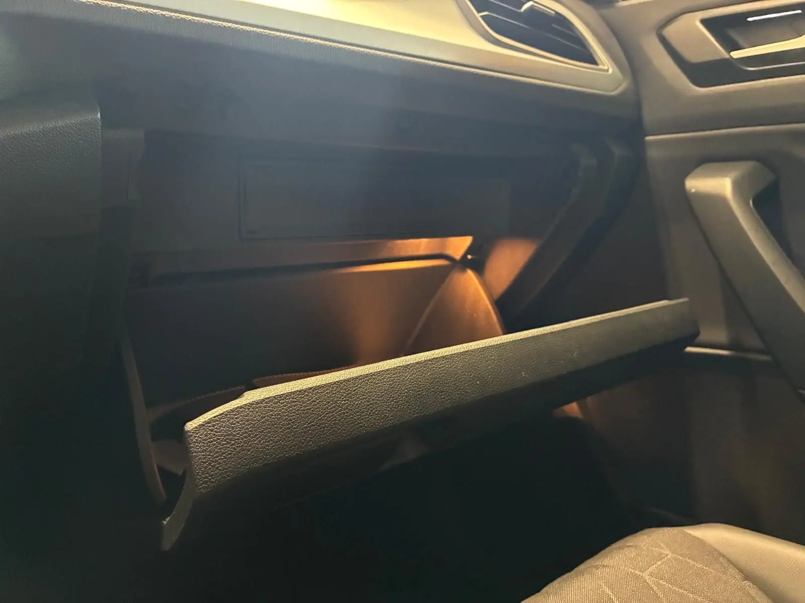 Gros plan intérieur sur la boîte à gants ouverte du Volkswagen T-Roc 2025, éclairage intérieur chaud visible.