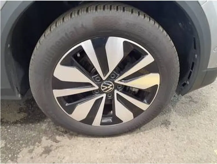Gros plan sur la roue avant droite d’un Volkswagen T-Roc gris clair, mettant en valeur la jante alliage bicolore au design moderne.