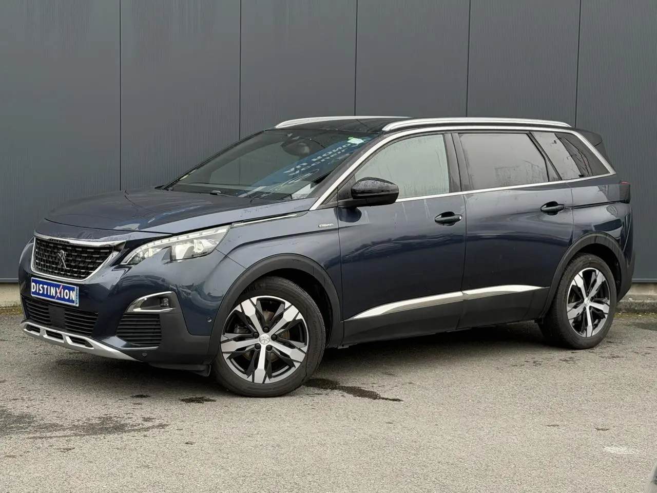 Peugeot 5008 bleu foncé en vue 3/4 avant droit, avec jantes alliage bi-ton et toit noir brillant.