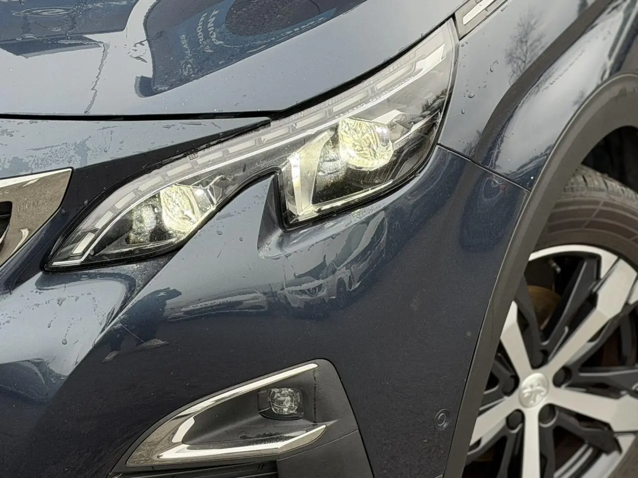 Gros plan sur l'avant droit du Peugeot 5008 bleu foncé, mettant en valeur le phare LED et la jante alliage bi-ton.
