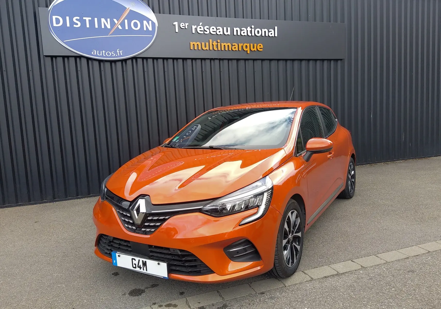 Renault Clio V E-Tech orange en 3/4 avant droit, avec calandre noire et jantes alliage bicolores.