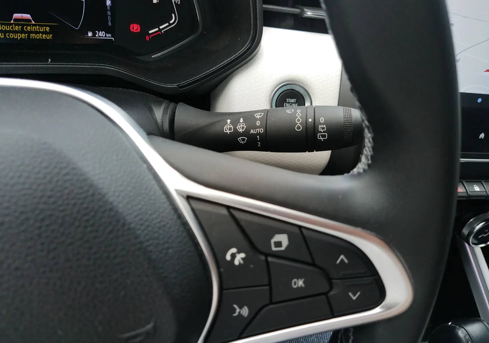 Gros plan sur le volant et la commande d’essuie-glace de la Renault Clio V E-TECH orange, intérieur noir et blanc.