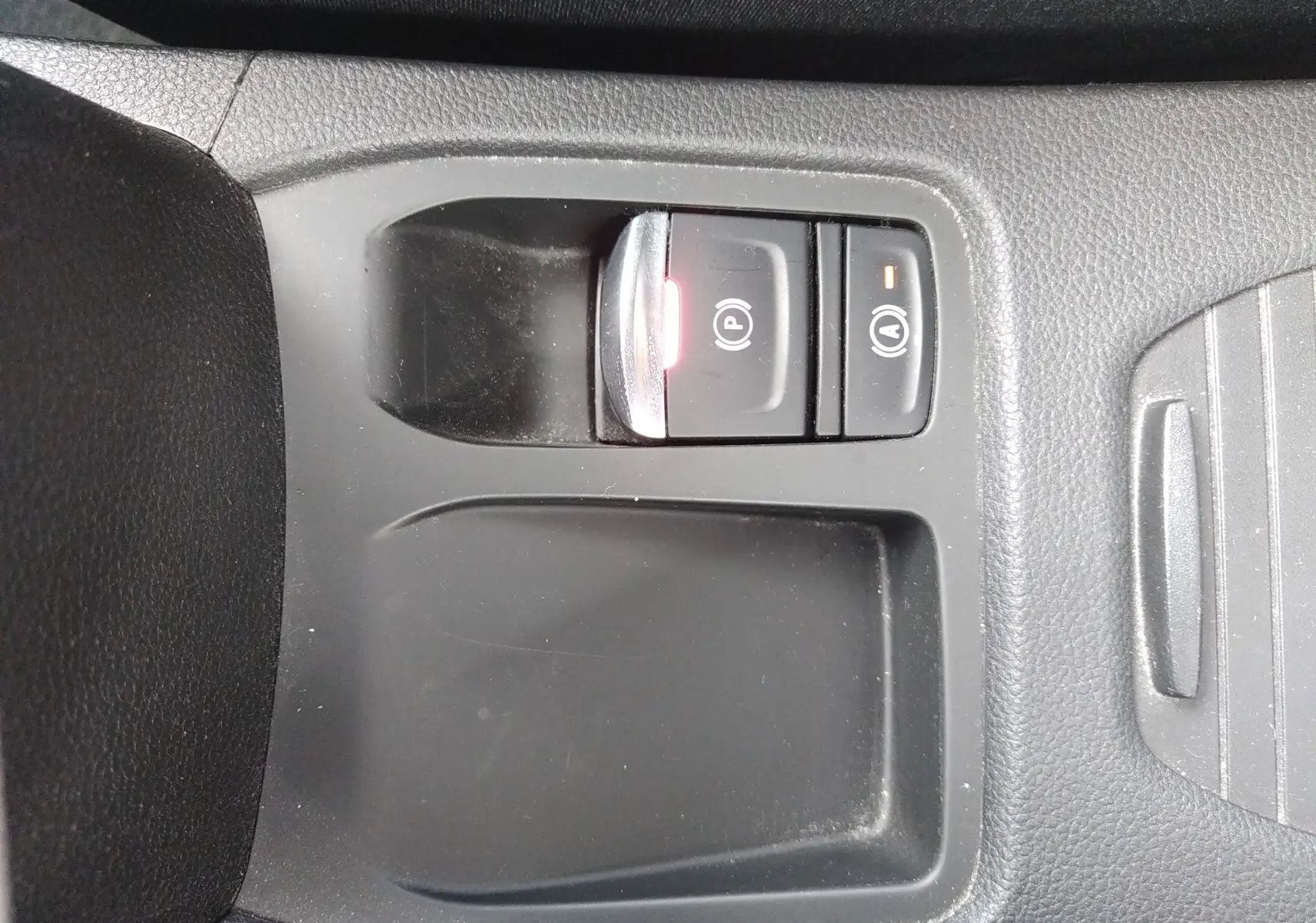 Gros plan sur les commandes de frein à main électrique et auto hold dans le console centrale noire d’une Renault Clio V orange.