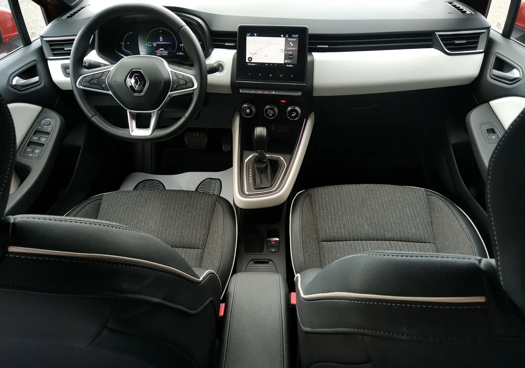 Vue intérieure avant de la Renault Clio V E-TECH 140ch, avec tableau de bord noir et blanc, écran tactile central et sièges tissu noir.